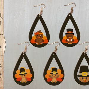 May include: Four pairs of laser cut wooden earrings featuring a Thanksgiving turkey design. Each earring is shaped like a teardrop and features a turkey with a pilgrim hat and a brown, orange, and yellow feather design.