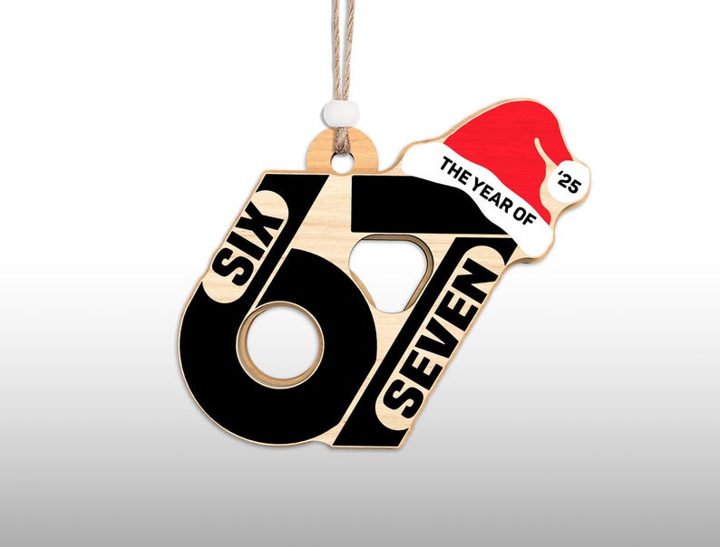 May include: Wooden Christmas ornament with the words "SIX" and "SEVEN" in black, forming the number 67. A red Santa hat with the text "THE YEAR OF '25" is on the top right. The ornament hangs from a natural-colored string.