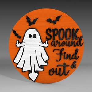 Op de afbeelding: Een rond houten bord met een oranje achtergrond en zwarte letters. Het bord toont een witte geest met zwarte ogen en een zwarte omtrek. De tekst op het bord luidt "Spook around Find out &".