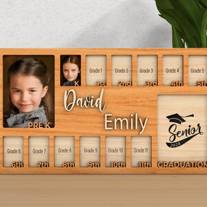 Pode incluir: Moldura de fotos de madeira com 11 slots para fotos, etiquetados com os graus desde o Pr&eacute;-K at&eacute; o 11&ordm; grau. A moldura tem o texto "David" e "Emily" escrito nela. O &uacute;ltimo slot tem um chap&eacute;u de formatura e o texto "Senior 2024" e "GRADUATION".