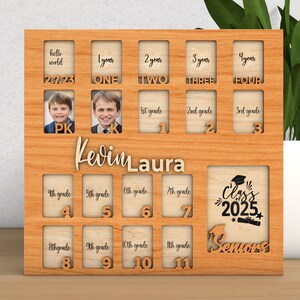 Pode incluir: Um porta-retratos de madeira com 16 slots para fotos, projetado para acompanhar o crescimento de uma crian&ccedil;a do jardim de inf&acirc;ncia ao ensino m&eacute;dio. O porta-retratos tem as palavras "Hello World", "Kevin Laura" e "Class of 2025" impressas nele.