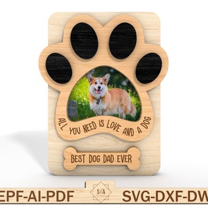 Puede incluir: Un marco de fotos de madera con forma de huella de pata con una foto de un perro en el centro. El marco tiene el texto "Todo lo que necesitas es amor y un perro" y "Mejor pap&aacute; de perro de todos los tiempos" grabado en &eacute;l.