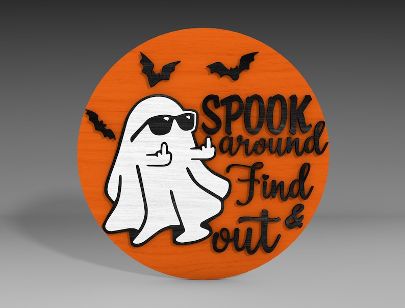 Op de afbeelding: Een rond, oranje houten bord met een zwarte geest die een zonnebril draagt en zijn middelvinger opsteekt. Het bord zegt "Spook around find out &" in zwarte letters.