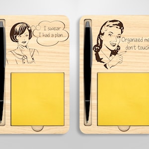 May include: A wooden desk organizer with two compartments, each with a notepad and a pen holder. The left compartment features a retro-style illustration of a woman with the text "I swear I had a plan..." The right compartment features a retro-style illustration of a woman with the text "Organized mess, don't touch."