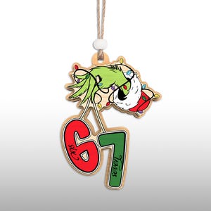May include: Wooden Christmas ornament featuring a green character with a Santa hat and string lights. The ornament has the numbers 6 and 7 in red and green, with the words "Six" and "Seven" on the numbers. A string is attached for hanging.