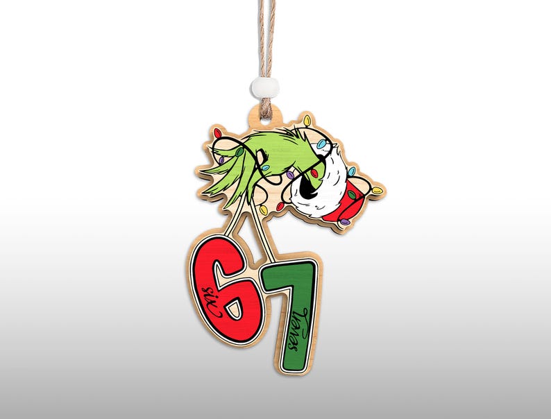 May include: Wooden Christmas ornament featuring a green character with a Santa hat and string lights. The ornament has the numbers 6 and 7 in red and green, with the words "Six" and "Seven" on the numbers. A string is attached for hanging.