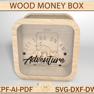 May include: A wooden money box with a clear front panel. The box has a design of mountains and the text "Let's go on an adventure" with an arrow pointing to the right.