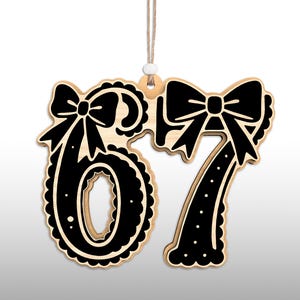 May include: Wooden ornament featuring the numbers 67 in a black and natural wood color scheme. Each number is adorned with a decorative bow. The ornament hangs from a natural twine string with a small white bead.