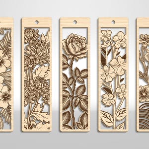 May include: Five wooden bookmarks with intricate floral designs. Each bookmark features a different flower, including hibiscus, chrysanthemums, a rose, and other blossoms. The bookmarks have a rectangular shape with a hole at the top for a tassel.