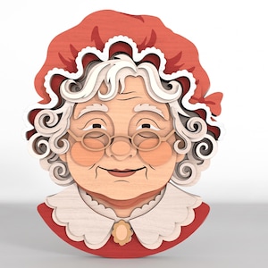 May include: A layered wooden wall art piece depicting an elderly person with white curly hair, wearing a red bonnet with a white ruffled trim, round glasses, and a white scalloped collar with a small central brooch over a red garment.
