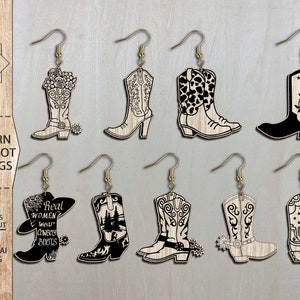 May include: Ten pairs of laser cut wooden cowgirl boot earrings. The boots are decorated with various designs, including floral patterns, cowboy boots, and the text "Real Women Wear Cowboy Boots".