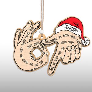 May include: Wooden Christmas ornament featuring a hand gesture with various slang terms. The ornament includes a Santa hat with the name "Jonathan" and the year "2025". It hangs from a string.