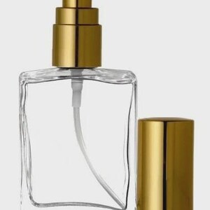 Może przedstawiać: Przezroczysty, kwadratowy szklany flakon perfum z rozpylaczem w kolorze złotym i oddzielną złotą nakrętką. Butelka ma białą plastikową rurkę i dyszę. Prosty i elegancki design.