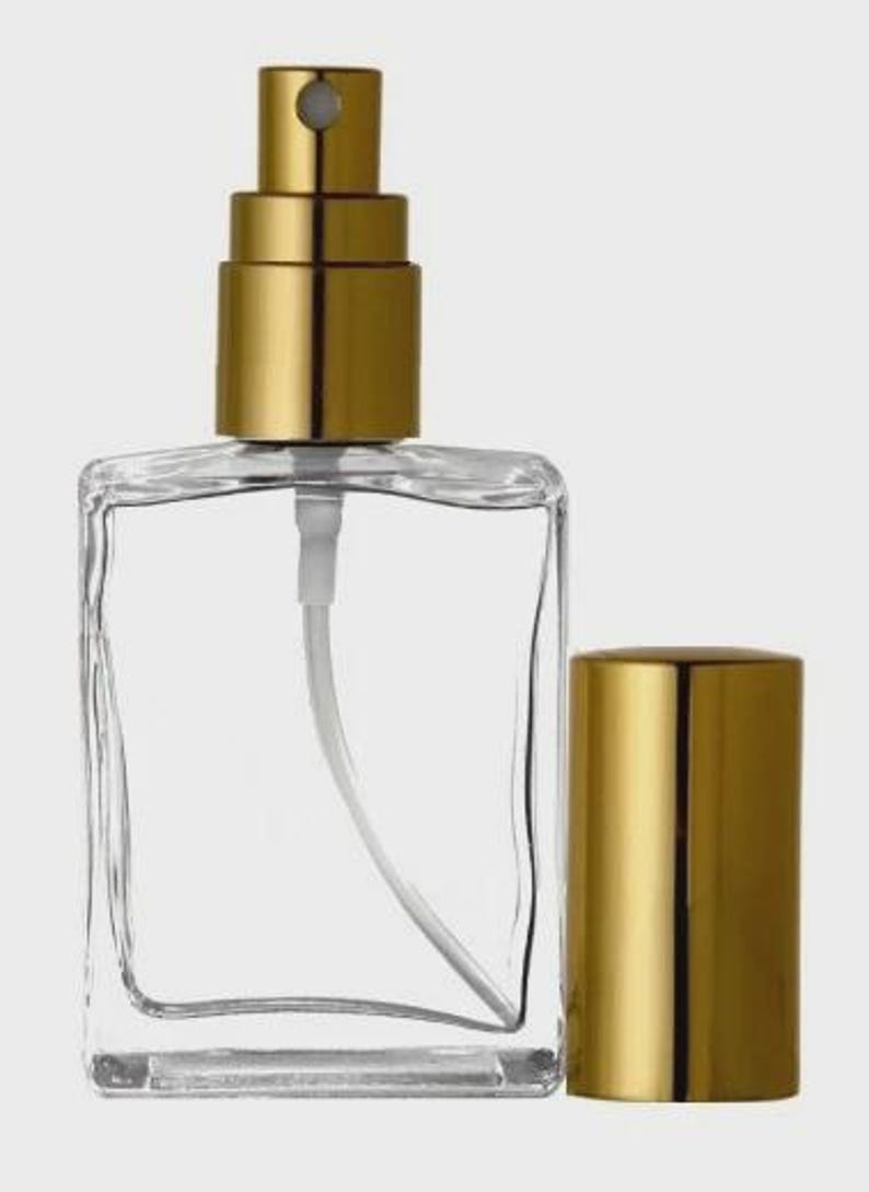 Może przedstawiać: Przezroczysty, kwadratowy szklany flakon perfum z rozpylaczem w kolorze złotym i oddzielną złotą nakrętką. Butelka ma białą plastikową rurkę i dyszę. Prosty i elegancki design.