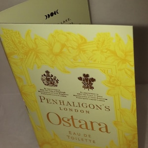Puede incluir: Caja amarilla y crema de Eau de Toilette Ostara de Penhaligon's. La caja presenta diseños florales y el texto "Ostara" en una fuente estilizada. Contiene 15 ml de perfume.