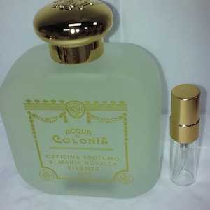 Puede incluir: Un frasco de perfume de vidrio esmerilado con tapa dorada y un pulverizador más pequeño a juego. La etiqueta dice "ACQUA di COLONIA" y "OFFICINA PROFUMO S. MARIA NOVELLA FIRENZE 1612".