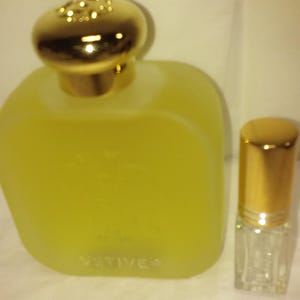 May include: Two bottles of perfume, one large and one small. The larger bottle is clear glass with a gold cap and the label "VETIVER". The smaller bottle is clear glass with a gold cap and a roller ball applicator.