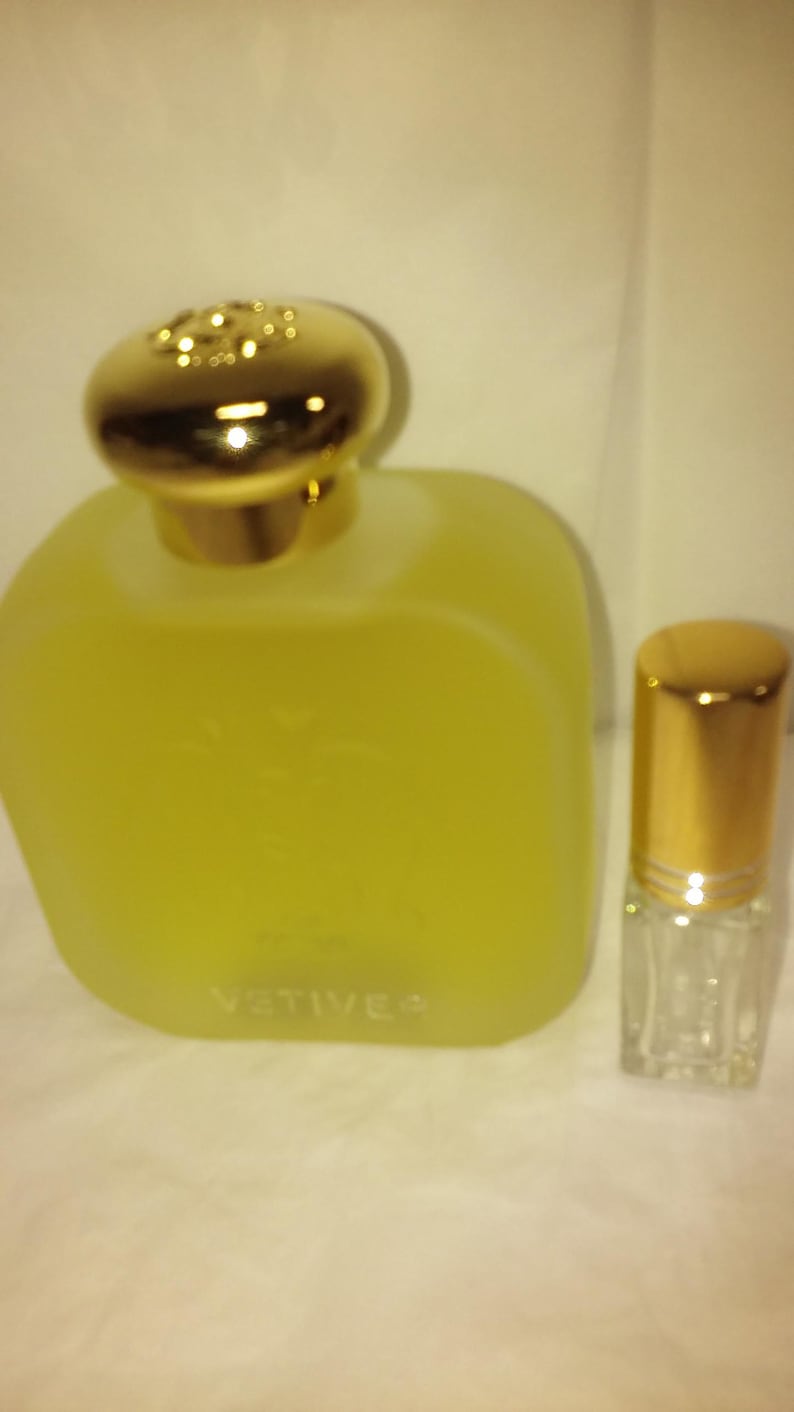 May include: Two bottles of perfume, one large and one small. The larger bottle is clear glass with a gold cap and the label "VETIVER". The smaller bottle is clear glass with a gold cap and a roller ball applicator.