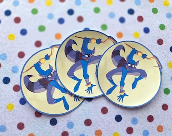 May include: Three round stickers featuring a cartoon raccoon character in shades of blue and yellow. The raccoon is depicted in a dynamic pose, holding a curved staff. The stickers have a blue border and are set against a polka dot background.