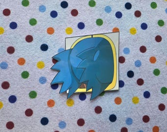 May include: A blue cartoon character sticker with a yellow border. The sticker has a stylized design with sharp, pointed edges. The background is a white fabric with colorful polka dots.