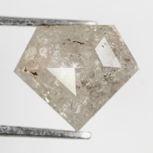 May include: A clear, faceted, gray diamond with inclusions, held by tweezers. The diamond is a square shape with a pointed top.