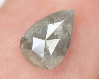 Puede incluir: Un diamante gris en forma de pera con un corte facetado. El diamante tiene un acabado rugoso y natural.
