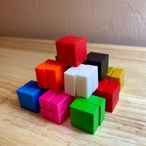 May include: A collection of colorful, small, cube-shaped toys in various colors, including red, orange, blue, pink, green, white, black, and yellow. The cubes are stacked on a wooden surface.