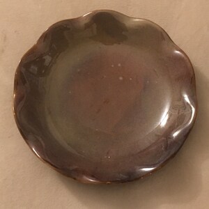 May include: A brown ceramic plate with a scalloped edge. The plate has a glossy finish and a subtle iridescent sheen.