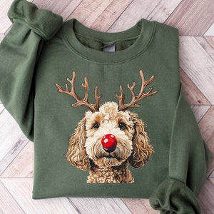 Op de afbeelding: Een militair groen sweatshirt met ronde hals en een grafische illustratie van een krulharige hond met bruine geweien en een felrode neus. De trui met lange mouwen heeft een geribbelde kraag, boorden aan de mouwen en een geribbelde zoom.