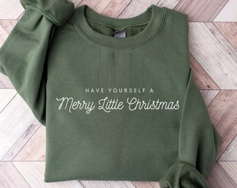 May include: An olive green crewneck sweatshirt featuring the white text "HAVE YOURSELF A Merry Little Christmas" printed on the front. The garment has long sleeves with ribbed cuffs and a ribbed neckline, showcasing a simple and clean design.