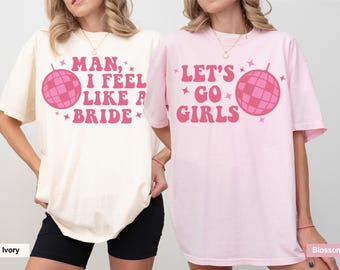 Puede incluir: Dos camisetas de manga corta con cuello redondo. La camiseta color marfil tiene el texto rosa Man, I Feel Like A Bride con una bola de discoteca. La camiseta rosa blossom tiene el texto rosa Let's Go Girls con una bola de discoteca y estrellas.