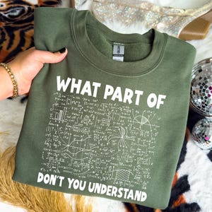 May include: An olive green sweatshirt with the text "WHAT PART OF DON'T YOU UNDERSTAND" in white. The text is surrounded by mathematical equations and symbols. The sweatshirt is a crew neck style.