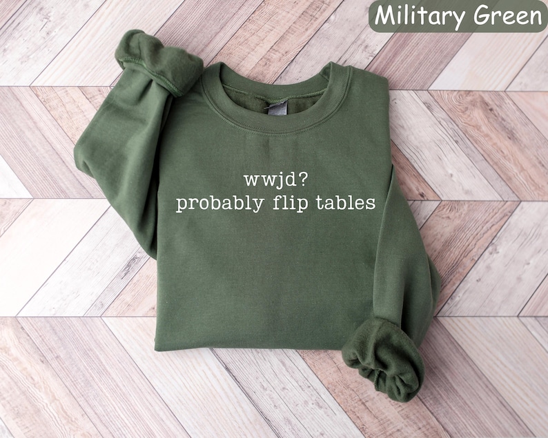 May include: Military green sweatshirt with the text "wwjd? probably flip tables" in white. The sweatshirt is made of a soft material and has a crew neck and long sleeves. The sleeves are cuffed at the wrists.