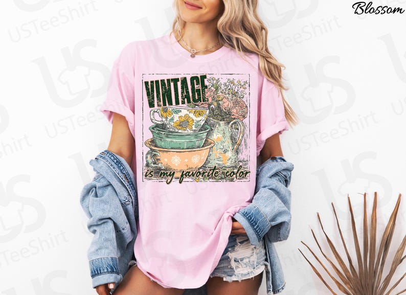 May include: Pink t-shirt with a graphic featuring stacked teacups, a pitcher of flowers, and the text "VINTAGE is my favorite color." The design has a vintage aesthetic.