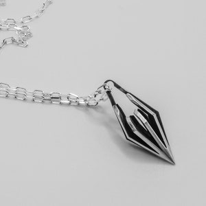 Puede incluir: Un collar de cadena de plata con un colgante de plata en forma de punta de flecha estilizada.