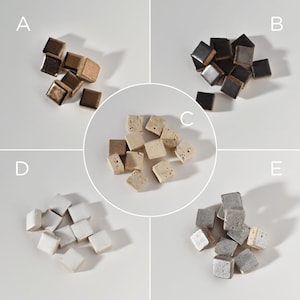 Könnte beinhalten: Sortiment kleiner quadratischer Keramikfliesen in fünf verschiedenen Farben: Gold, Schwarz, Beige, Weiß und Silber. Die Fliesen sind in Stapeln auf weißem Hintergrund angeordnet.