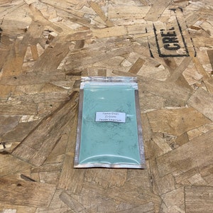 May include: A small resealable bag containing 25 grams of Cyprus Green powder pigment. The bag is on a wood surface. The label reads "Cyprus Green 25 Grams Powder Emporium".