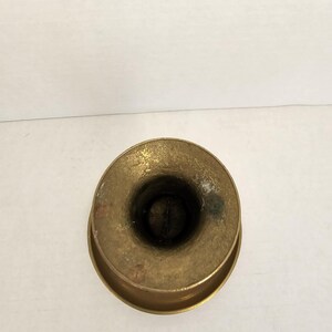 May include: A top-down view of a small, antique brass candle holder. The candle holder has a circular base and a cylindrical opening for the candle. The brass has a slightly tarnished appearance.