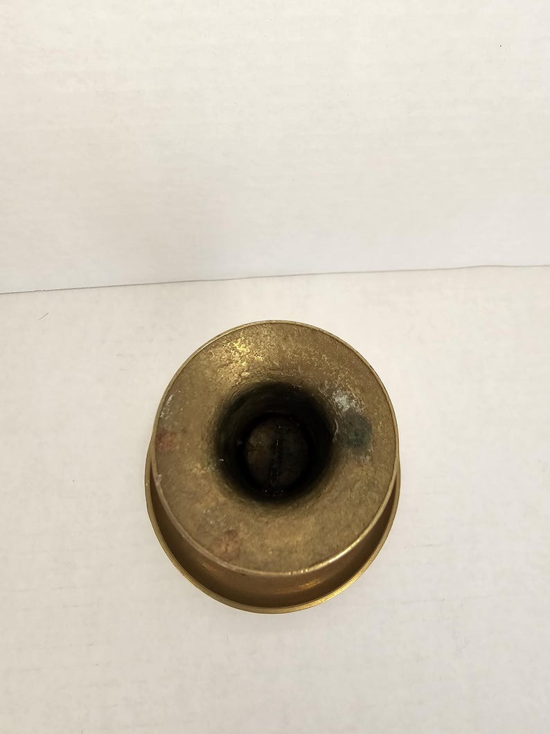 May include: A top-down view of a small, antique brass candle holder. The candle holder has a circular base and a cylindrical opening for the candle. The brass has a slightly tarnished appearance.