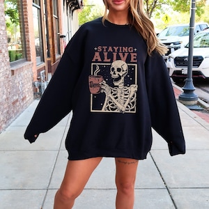 May include: Black sweatshirt featuring a skeleton holding a coffee cup with the text "Staying Alive".
