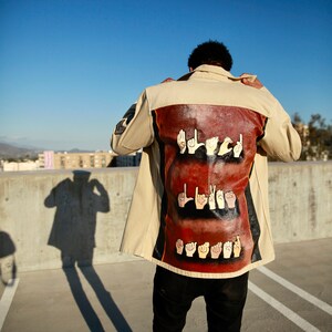 May include: A person wearing a beige jacket with a brown patch on the back. The patch features the words "Black Lives Matter" spelled out in American Sign Language.