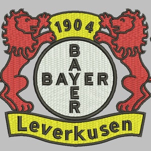 Op de afbeelding: Een geborduurde zwarte en witte patch met een rood en wit logo. Het logo toont twee rode leeuwen die een witte cirkel met de tekst "BAYER" in zwart flankeren. De tekst "1904" staat in zwart op een gele banner boven de cirkel. De tekst "Leverkusen" staat in zwart op een gele banner onder de cirkel.