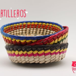 Puede incluir: Un conjunto de tres cestas tejidas de colores, apiladas una encima de la otra. Las cestas están hechas de materiales naturales y tienen una variedad de colores brillantes, incluyendo rojo, amarillo, azul, verde y negro. Las cestas están etiquetadas como "Tortilleros".
