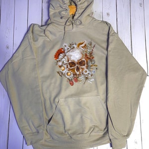 May include: A beige hooded sweatshirt with a skull surrounded by flowers, mushrooms, and insects printed on the front.