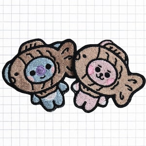 May include: Two embroidered patches featuring cartoon characters wearing brown and tan fish-shaped costumes. The character on the left is blue with a purple nose and the character on the right is pink with a red nose.