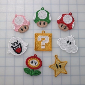 Peut inclure: Neuf patchs brodés représentant des personnages et des objets de la série de jeux vidéo Super Mario Bros. Les patchs sont blancs, rouges, verts, jaunes et dorés. Les personnages incluent un fantôme, un champignon et une étoile. Les objets incluent un bloc question et une fleur.