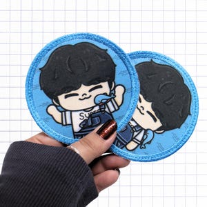 May include: Two circular embroidered patches featuring a cartoon character with black hair, wearing a white shirt with the text Super and dark blue overalls. The character is surrounded by a light blue background with small blue whale illustrations.