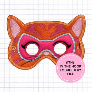 May include: An orange and pink felt cat mask featuring embroidered details, including a light blue outline around the eye holes, black eyelashes, and whiskers. A pink circular graphic overlay contains the text (ITH) IN THE HOOP EMBROIDERY FILE.