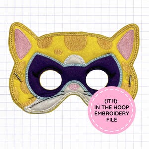 May include: A yellow felt cat mask with orange spots, pink inner ears, and a purple eye patch. The mask features embroidered details, including black eyelashes and whiskers. A pink circle overlay contains the text (ITH) IN THE HOOP EMBROIDERY FILE.
