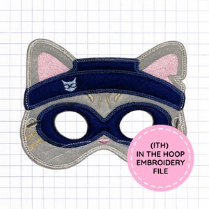 May include: A gray felt cat mask featuring a dark blue ninja headband with a small white cat icon and a dark blue eye mask overlay. The ears have pink accents, and the face includes gold stitched whiskers. Text reads (ITH) IN THE HOOP EMBROIDERY FILE.